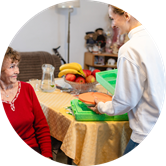 A caregiver provides a meal to an older woman in her home. A caregiver provides a meal to an older woman in her home.