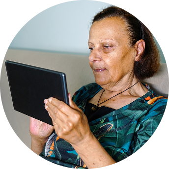 A woman sits on a couch while looking at a tablet. 
