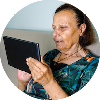 A woman sits on a couch while looking at a tablet. 