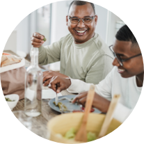 Two men smile and eat a meal at a table Providing Nutritious Meals to People Image