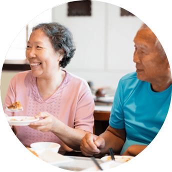 An older man and woman eat a meal at the table while smiling Share Your Story Desktop Image