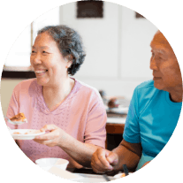 An older man and woman eat a meal at the table while smiling Share Your Story Mobile Image